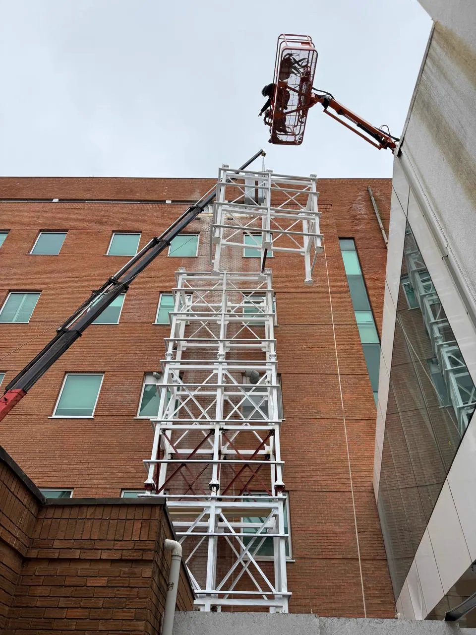 Grúa izando un módulo de estructura metálica mientras un operario trabaja desde un alzahombre