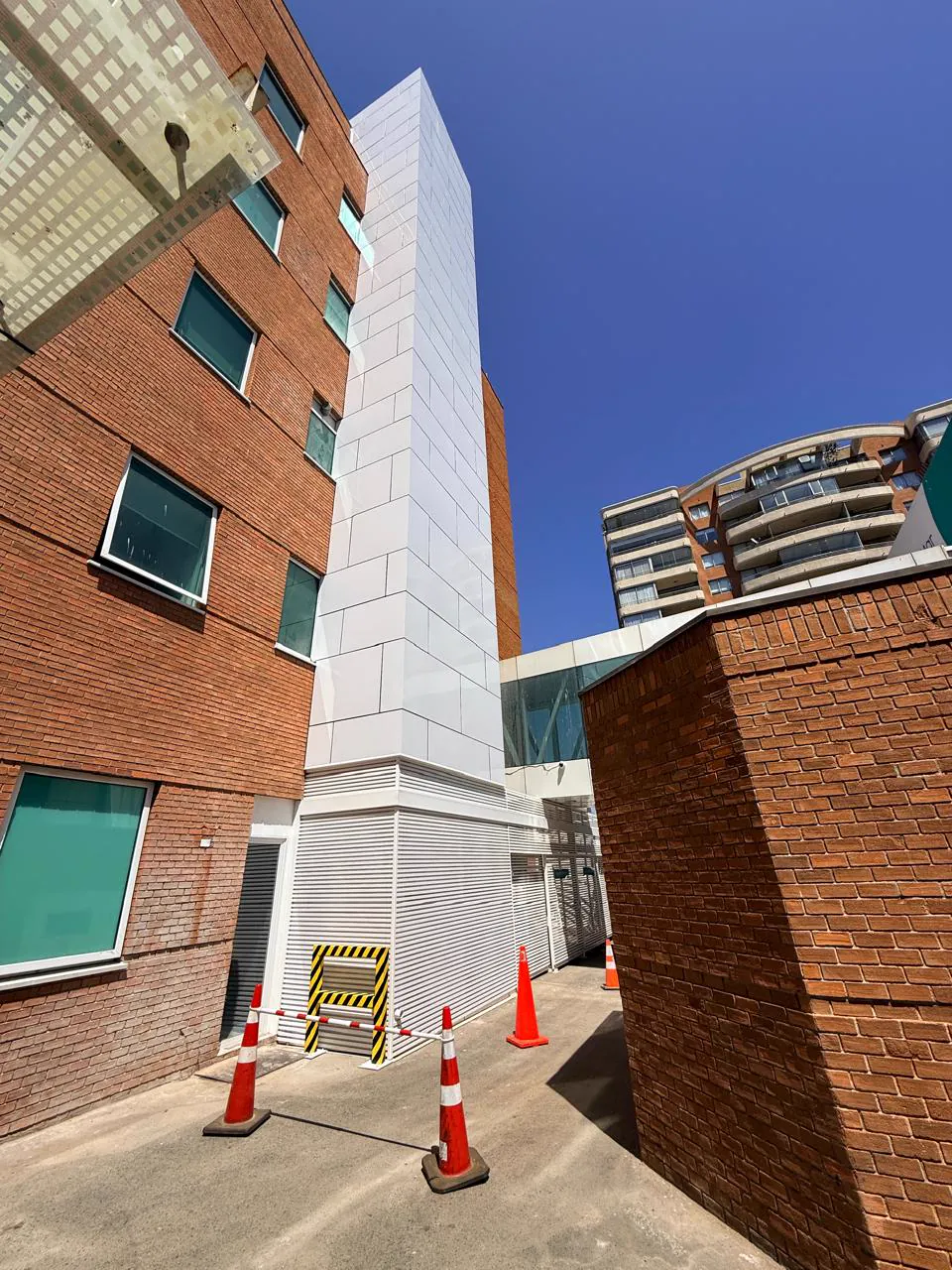 Torre de estructura metálica revestida en blanco, adosada a la fachada de ladrillo de un edificio